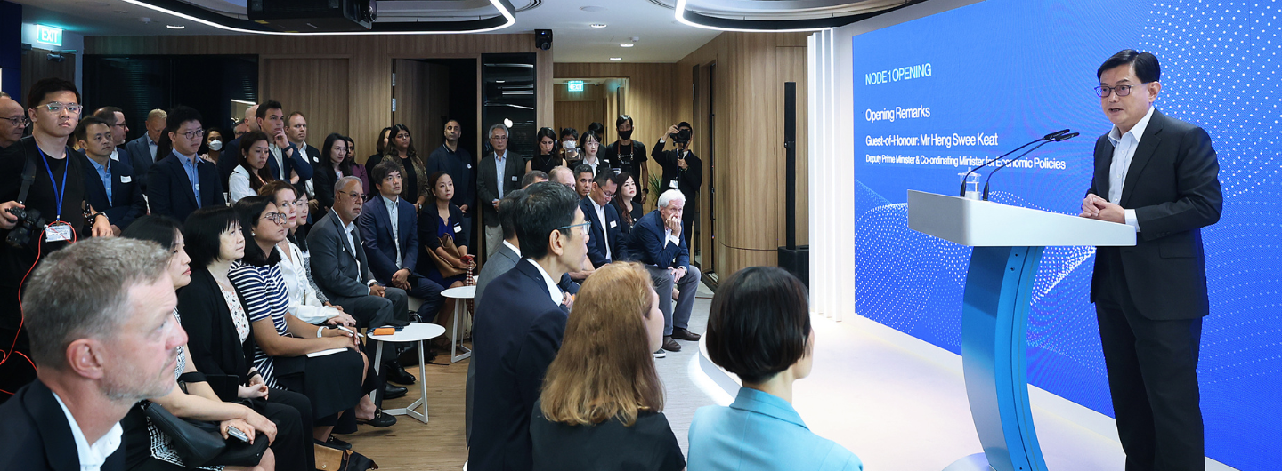 Heng Swee Keat speaks at podium before an audience; screen reads "NODE 1 OPENING".
